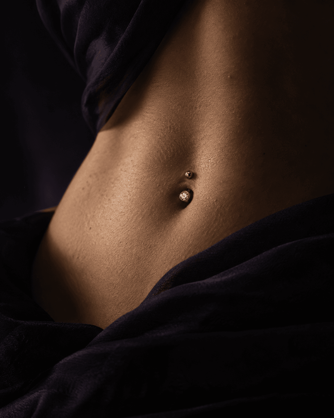 Detalhe de piercing de umbigo em titânio com iluminação lateral.