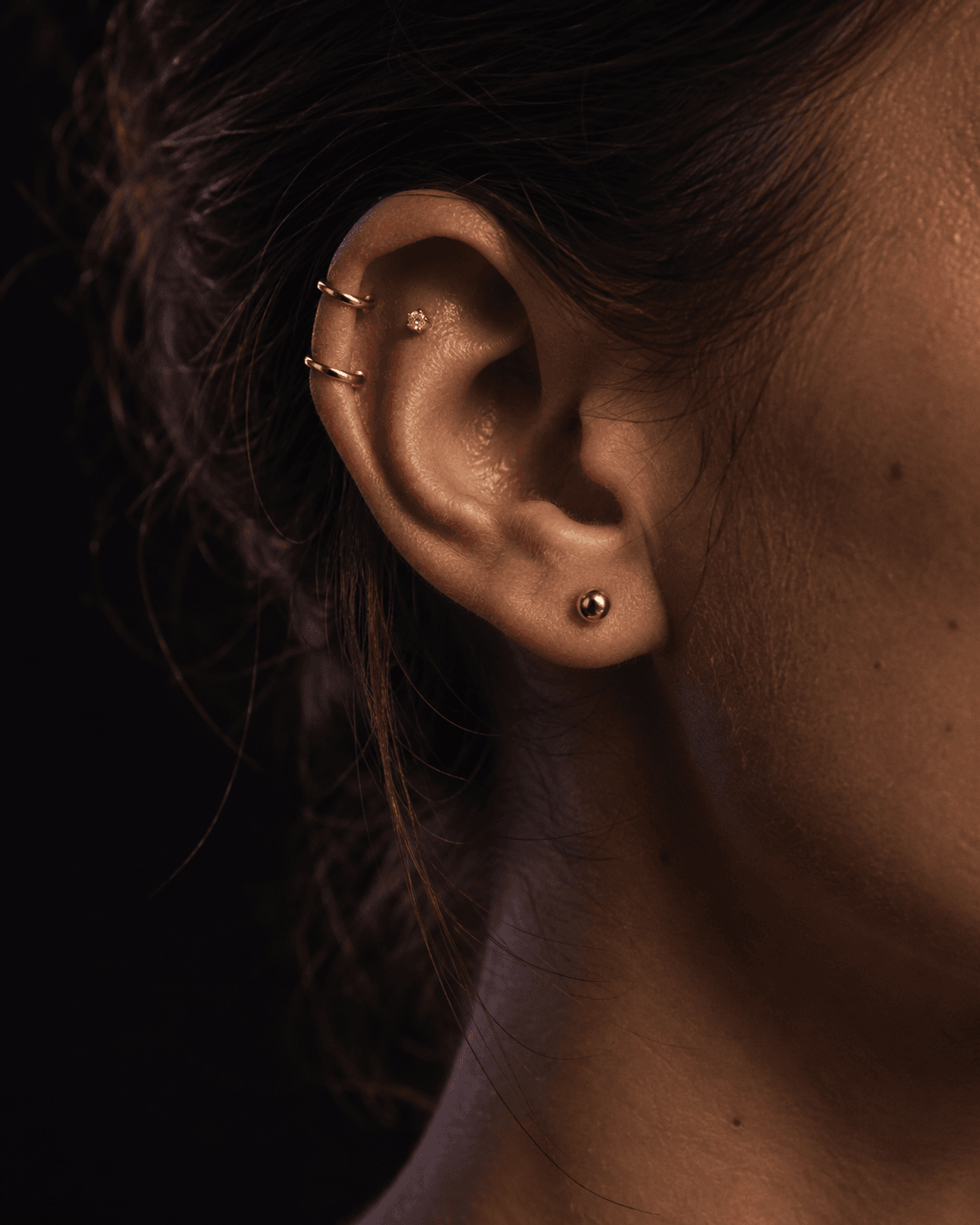 Orelha com composição de piercings em ouro: helix, flat e lóbulo.