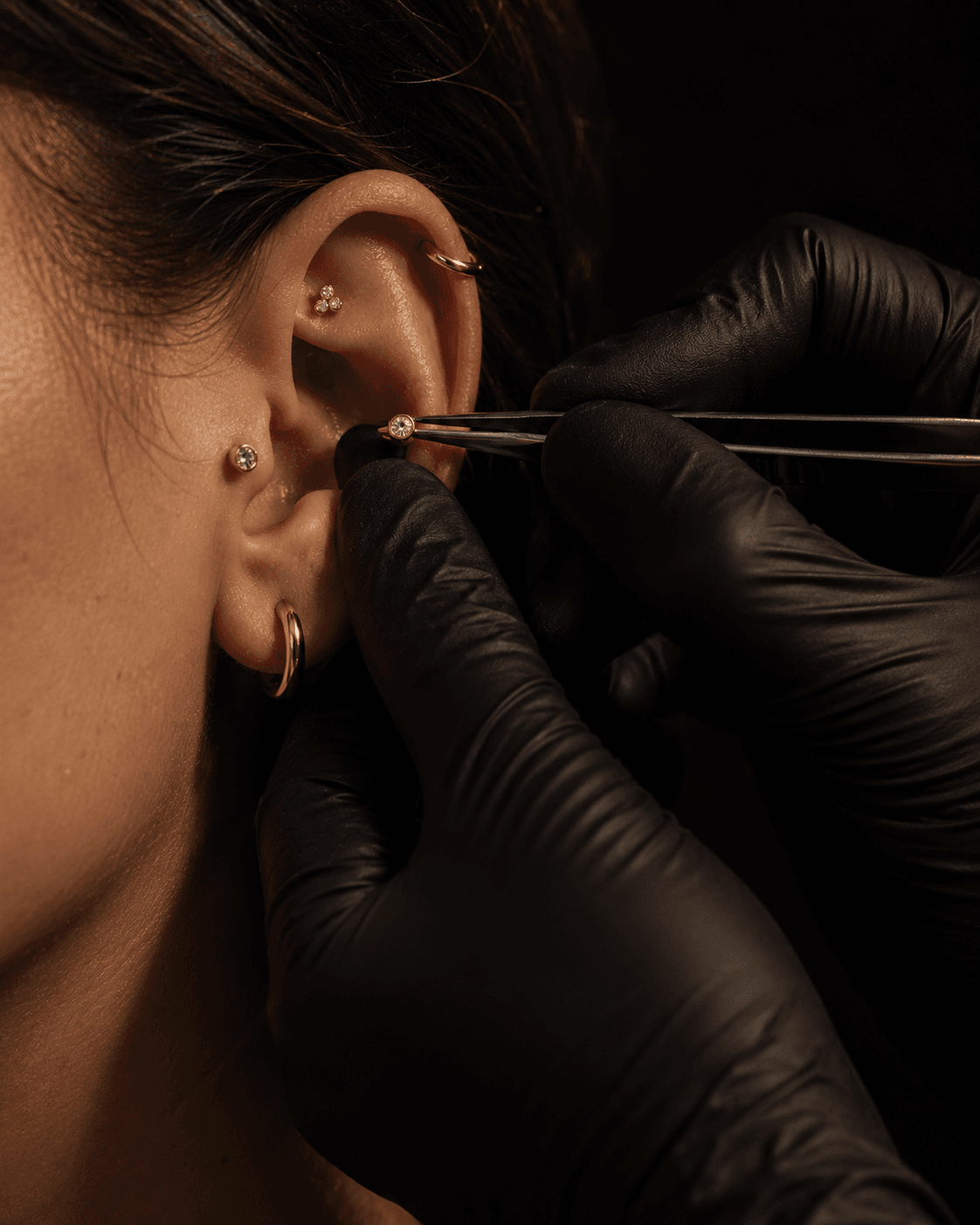 Mãos com luvas trocando uma joia de piercing com precisão.